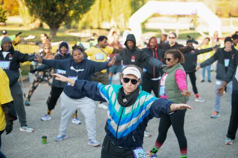 A group of 5K participants stretch with their arms out and their feet apart.