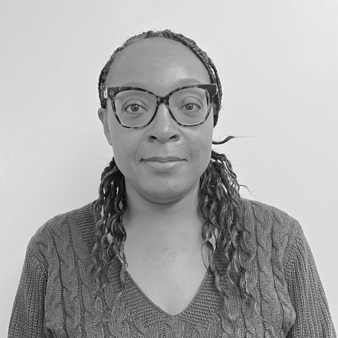 A black and white headshot of a dark-skinned woman with glasses and long hair.
