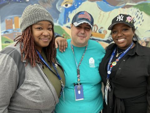 A dark-skinned woman with a gray beanie, a medium-skinned man with a denim baseball cap and a dark-skinned woman with a black baseball cap