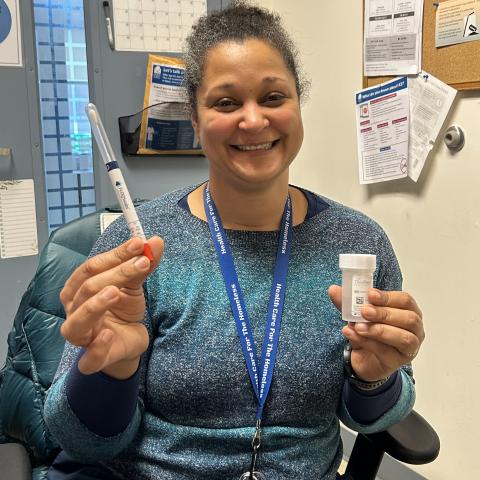 A woman holds an HPV self-swab test tube and a container of solution.