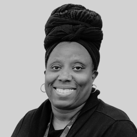 A black and white headshot of a smiling dark-skinned woman wearing a dark head wrap.