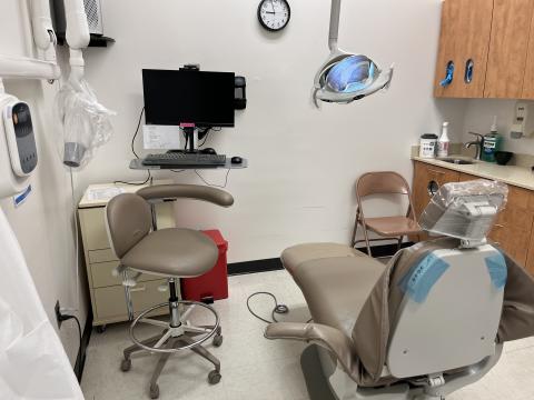 Room with a dental chair, computer and chair.