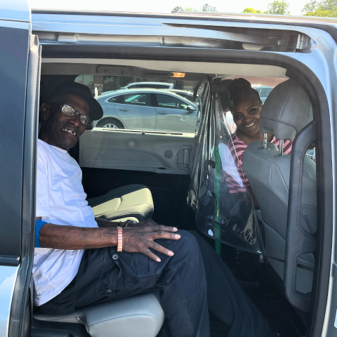 Two people smile inside a car with the door open.