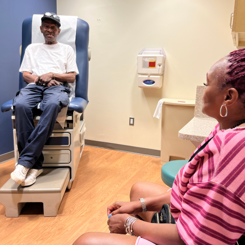 A woman sits in a doctor's office looking at a man in an exam chair.