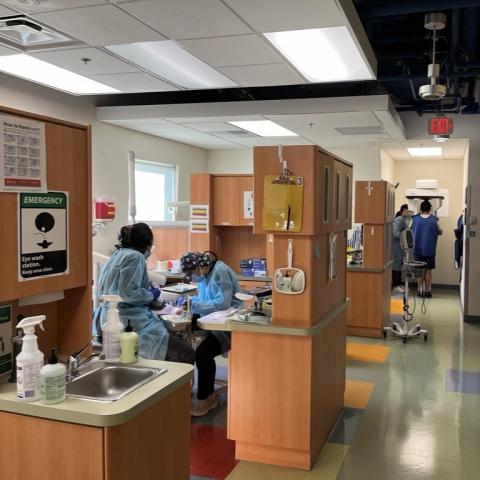 Dental staff work on a client in the foreground while another client received an x-ray in the background.