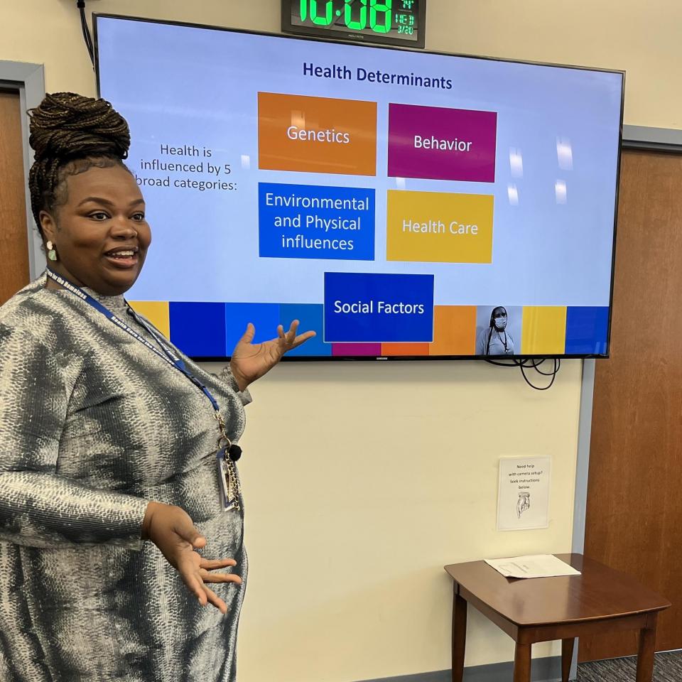 Black woman smiling as she presents a powerpoint about health determinants