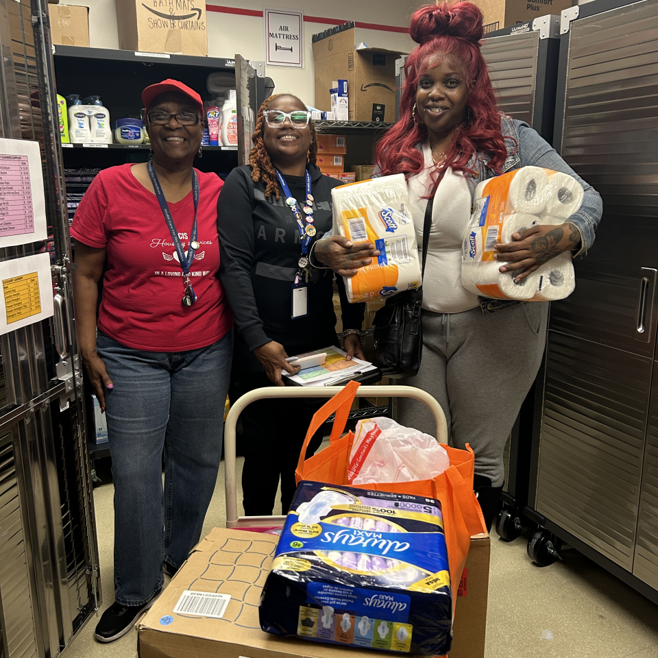 Three people smile and stand in the Home Starter Kit store behind a cart loaded with boxed.