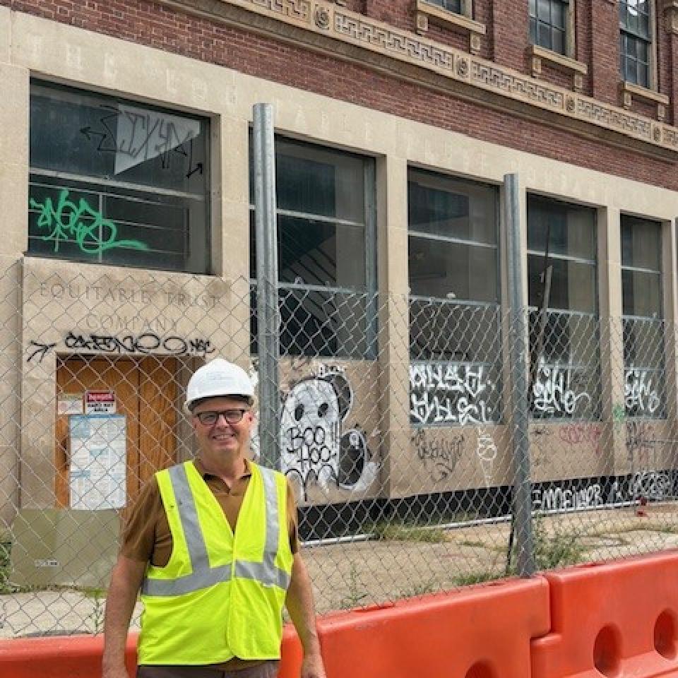 A light-skinned man in a hard hat and vest standings in front of the future site of Sojourner Place at Park.