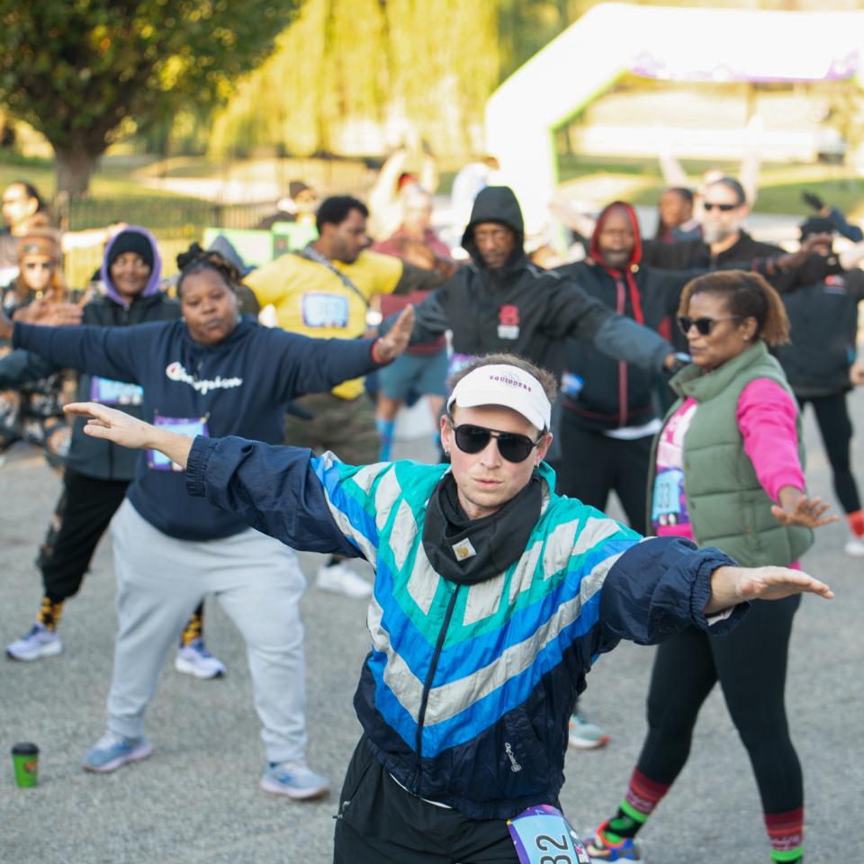 A group of 5K participants stretch with their arms out and their feet apart.
