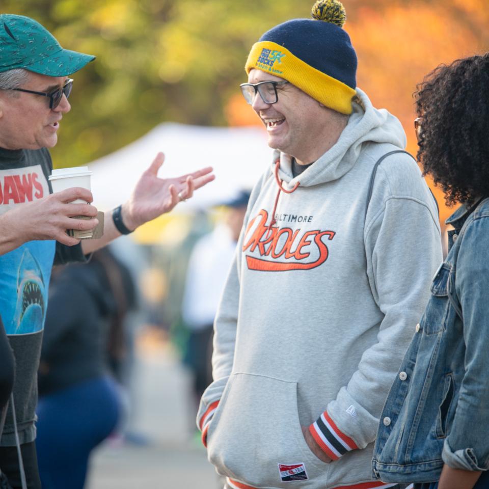Two light-skinned men in hats and glasses engage in conversation outside