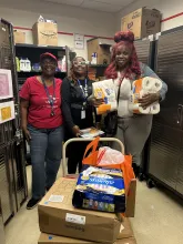 Three people smile and stand in the Home Starter Kit store behind a cart loaded with boxed.
