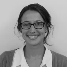 A black and white headshot of a light-skinned woman with glasses and hair pulled back.