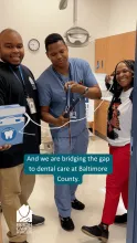 A gif of three adults inside a dental suite. Two hold oversized dental floss across the door frame while the man in the middle cuts the floss with oversized scissors. They celebrate!