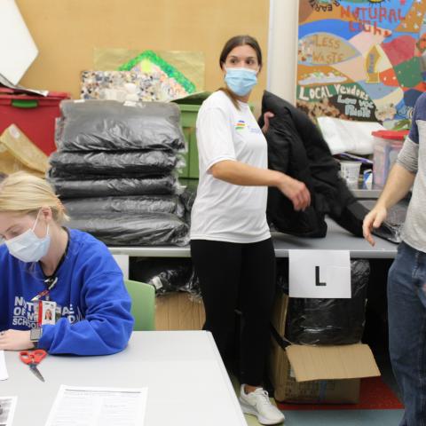Nursing students, Constellation employees, and other volunteers help hand out coats. A light skinned person with a white 
