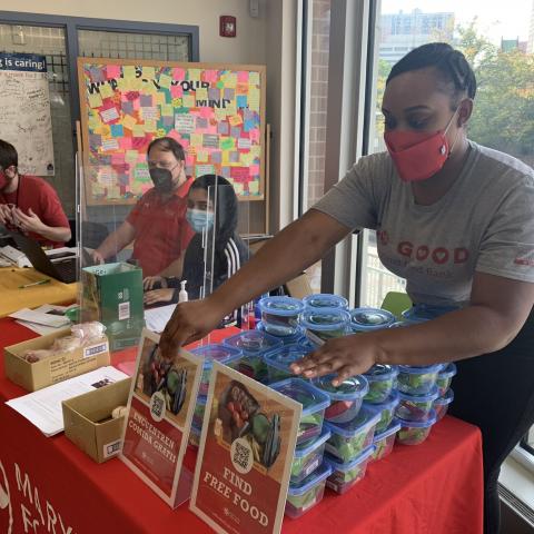 Several Maryland Food Bank staffers, with varying skin tones and wearing face masks, setting up a display of information and free snacks. 